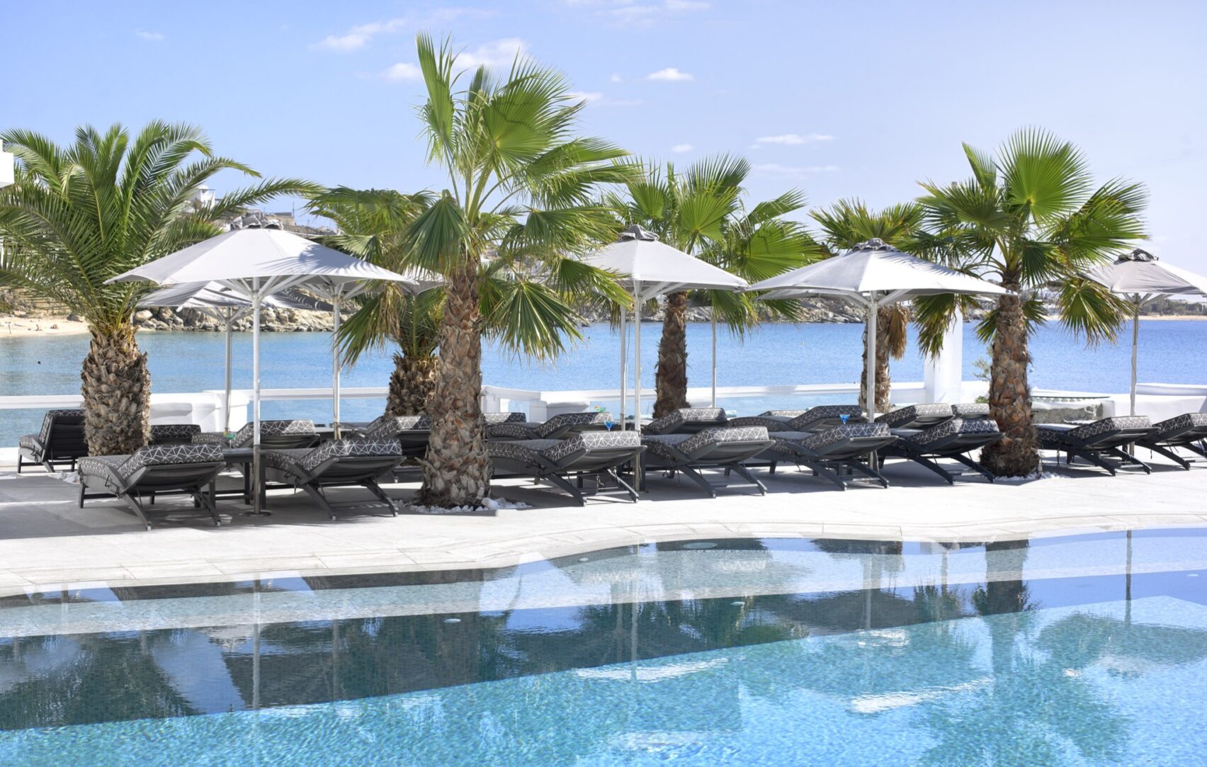 Piscine et transats, parasols et pieds dans l'eau pour le Petinos Beach 4étoiles sur l'île de Mykonos dans les Cyclades en Grèce