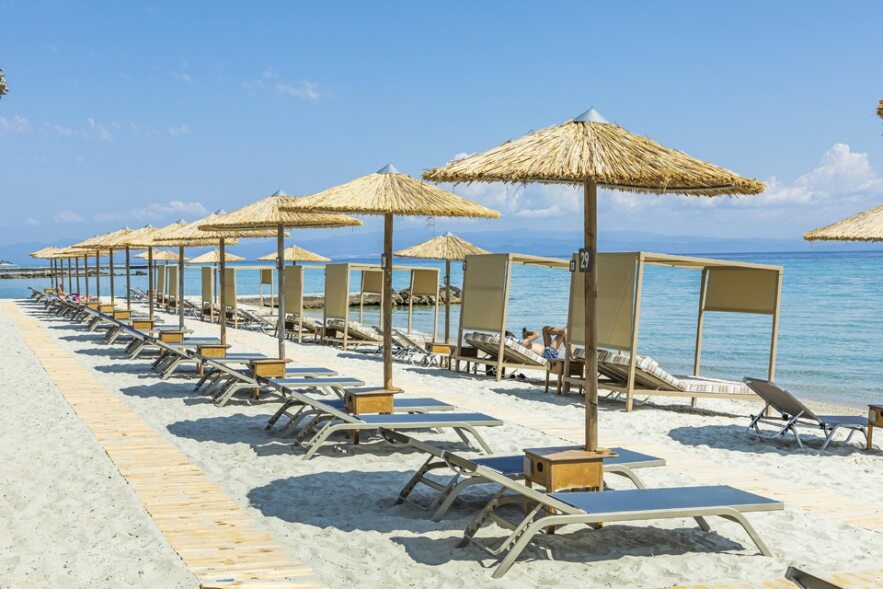 Plage de sable blond avec parasols et chaises longues ainsi que placebots devant l'hôtel Ammon Zeus situé à Kallithea en Chalcidique en Grèce du nord