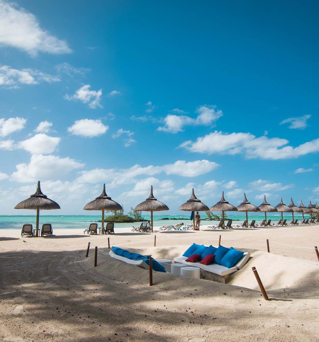 Bord de mer avec parasol authentiques et chaises longues à la plage de l'hôtel La Pirogue 4*Luxe à l'île Maurice